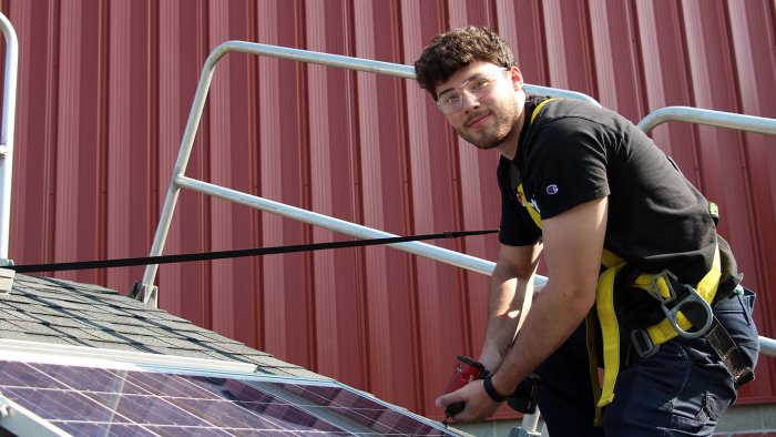 Student works on a solar panel on a roof