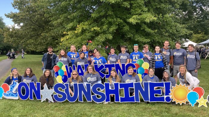 Student stand behind Walking on Sunshine sign