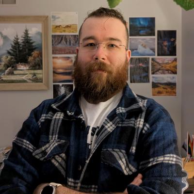 Jeremy Howard, a white man with short curly hair, a ginger beard, and glasses, smiling with his arms crossed, wearing a blue and white flannel and an alfred state tshirt, standing in front of a collage of nature photography and a painting of the Swiss Alps.