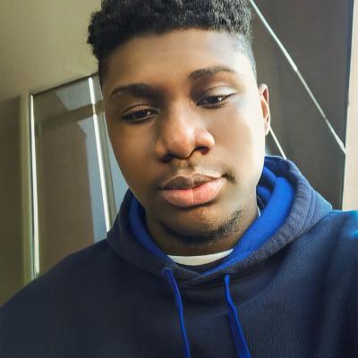 A photo of Xavier Andrews in a navy and royal blue hoodie sits near a window, looking relaxed with a soft expression.