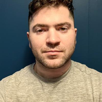 A headshot of Eric Scouten with short, wavy brown hair and a neatly groomed beard. He is wearing a light gray shirt and is set against a solid, dark blue background, creating a clean and modern aesthetic.