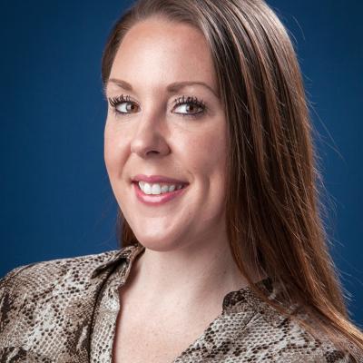 A photo of Christine Reynolds with long brown hair, wearing a patterned blouse. The background is a solid blue.