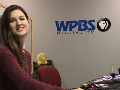 Leah sitting in front of a computer, WPBS logo on wall
