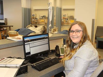 Raeha sitting at a desk with laptop in a hospital setting