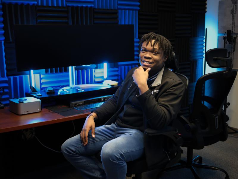 student smiles while sitting in a recording studio