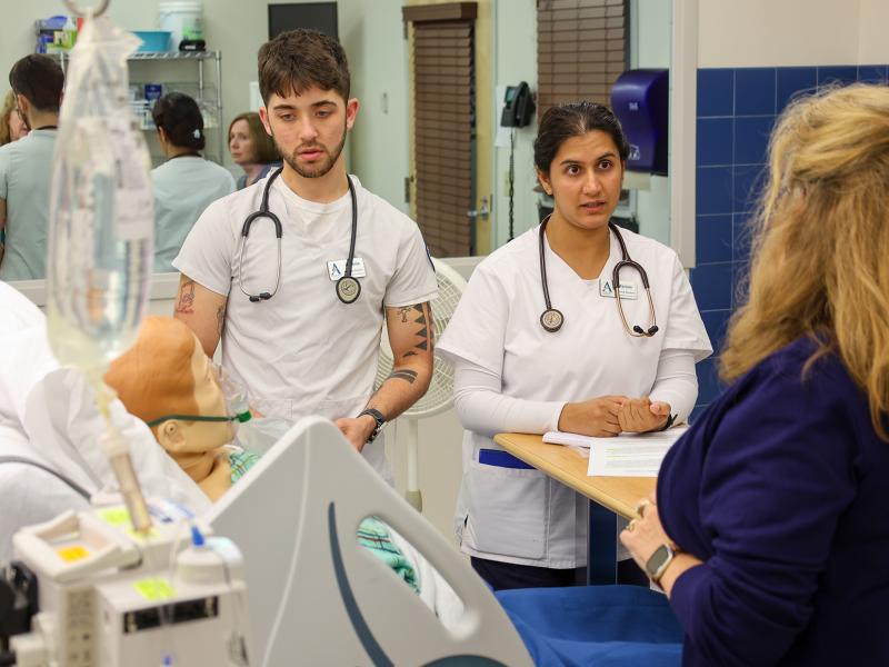 students work with a professor in a nursing lab