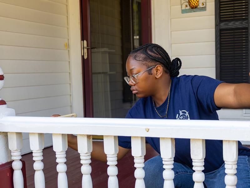student paints a railing for a resident