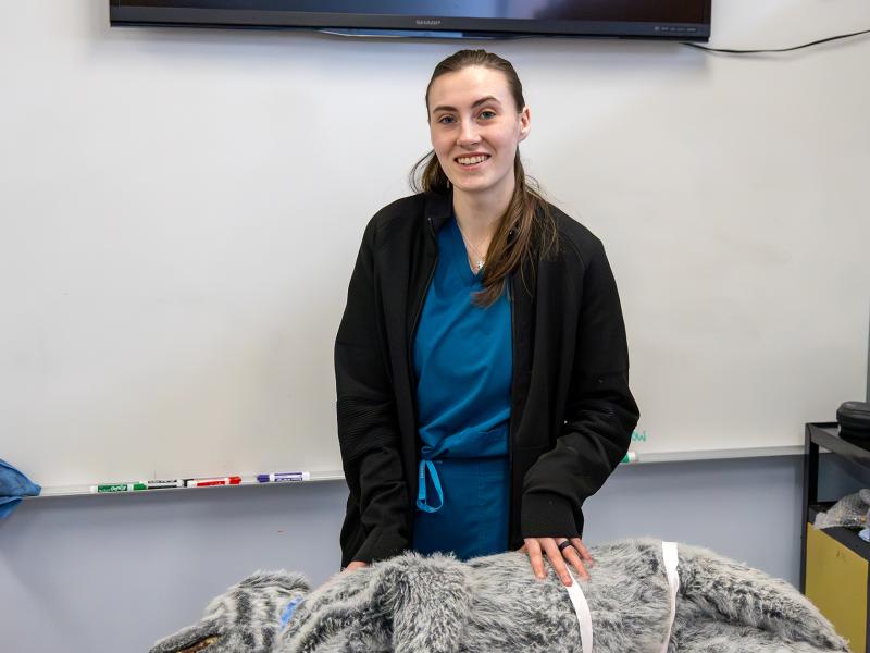 student stands in vet tech lab with manikin animal