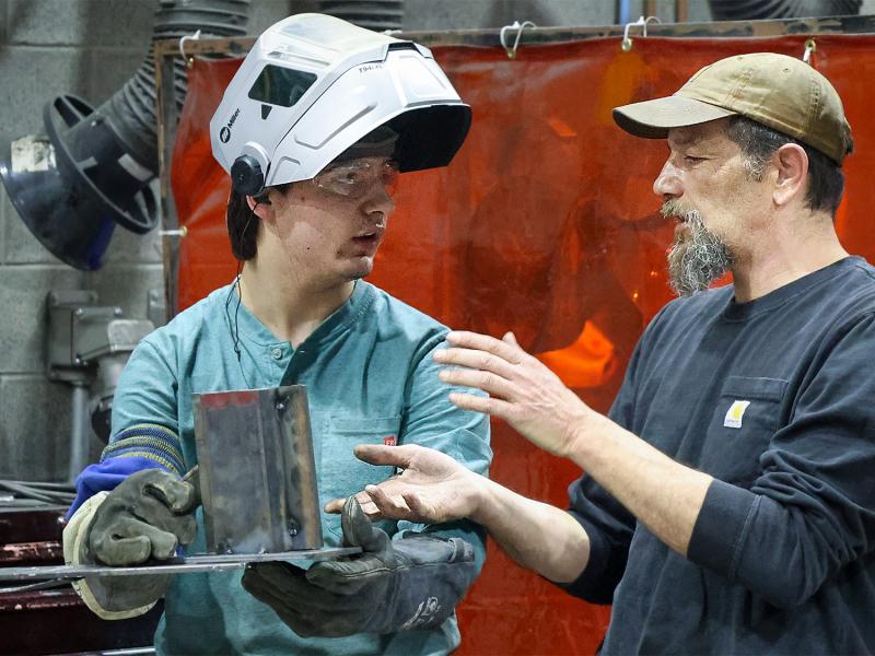 Professor speaks with a student in a welding lab