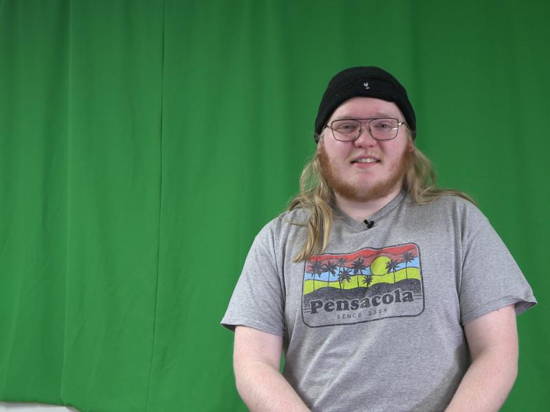 student sits in front of a green screen