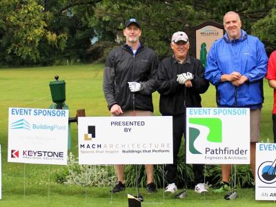 A foursome stands in front of tournament sponsor signs at the Alfred State Golf Tournament