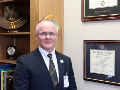 Jim Helms stands near his Alfred State diploma