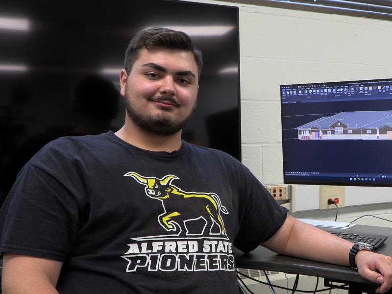 student poses in a lab with a computer screen displays a drawing