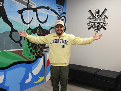 Gabriel Dueño stands in front of the mural in Pioneer Cuts, the new barbershop at Alfred State located in Pioneer Center. 
