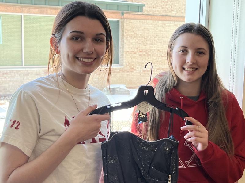 Pair of Delta Chi Omega sisters hold up a dress
