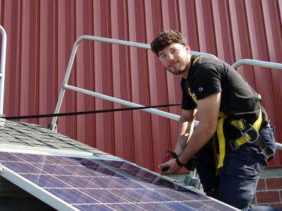 Student works on a solar panel on a roof