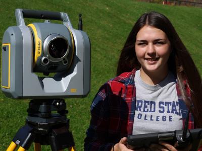 Students stands with surveying equipment