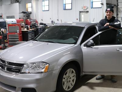 A student stands with the 2014 Dodge Avenger