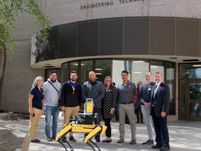 Group of individuals standing in front of building behind Spot the robot dog
