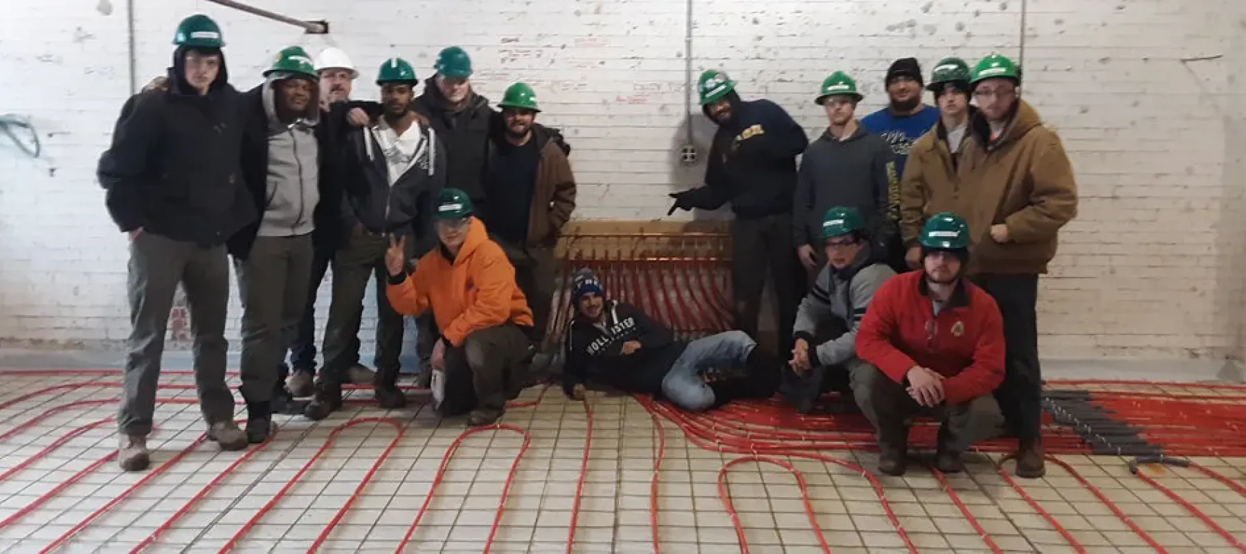 Students posing in building with multiple small pipes running along the floor.