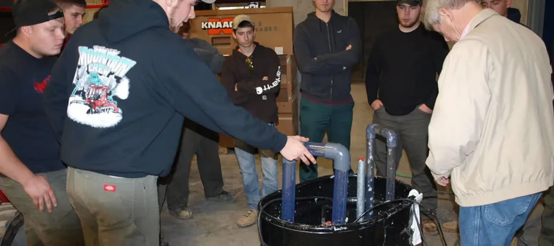 Students gathered around demonstration with various connected pipes.