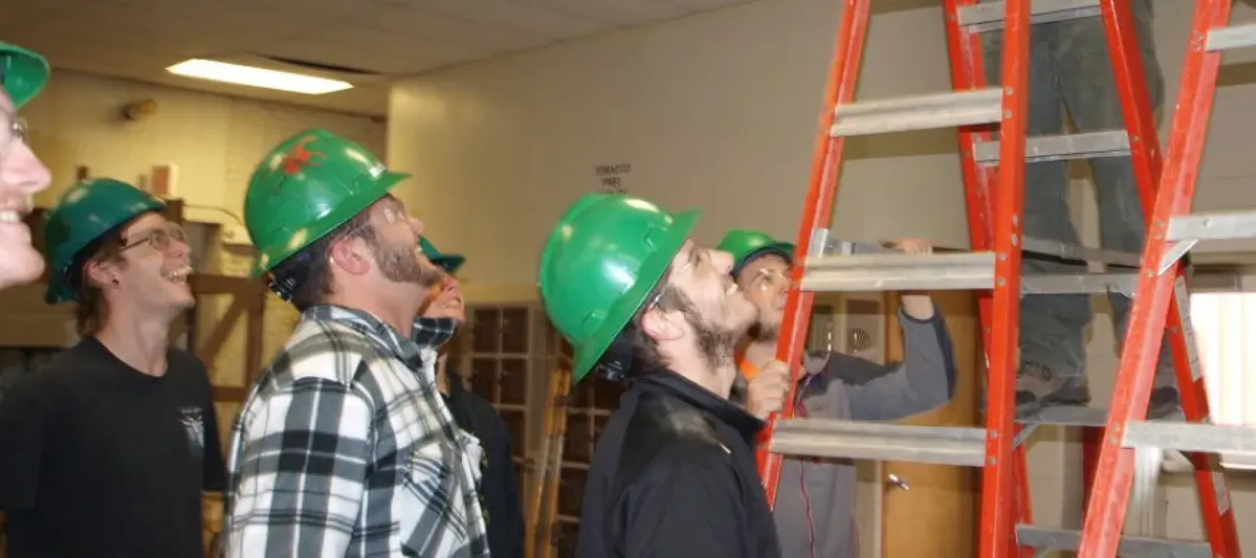 Students look up towards man on ladder inside building.