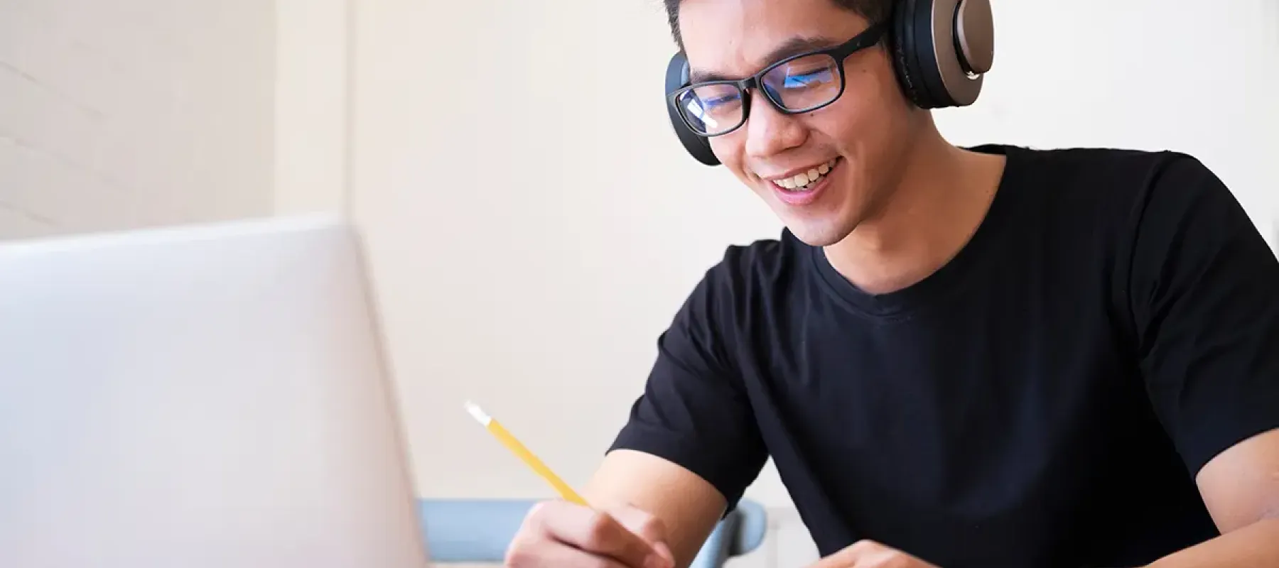 Online student sitting in front of laptop and wearing headphones taking notes.