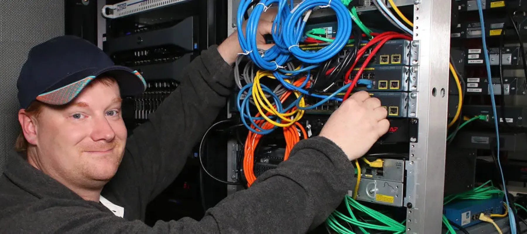 Student connecting ethernet cables to network switch on rack.