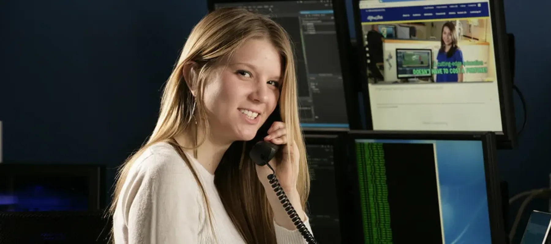 Student on landline phone with computer screens in background.
