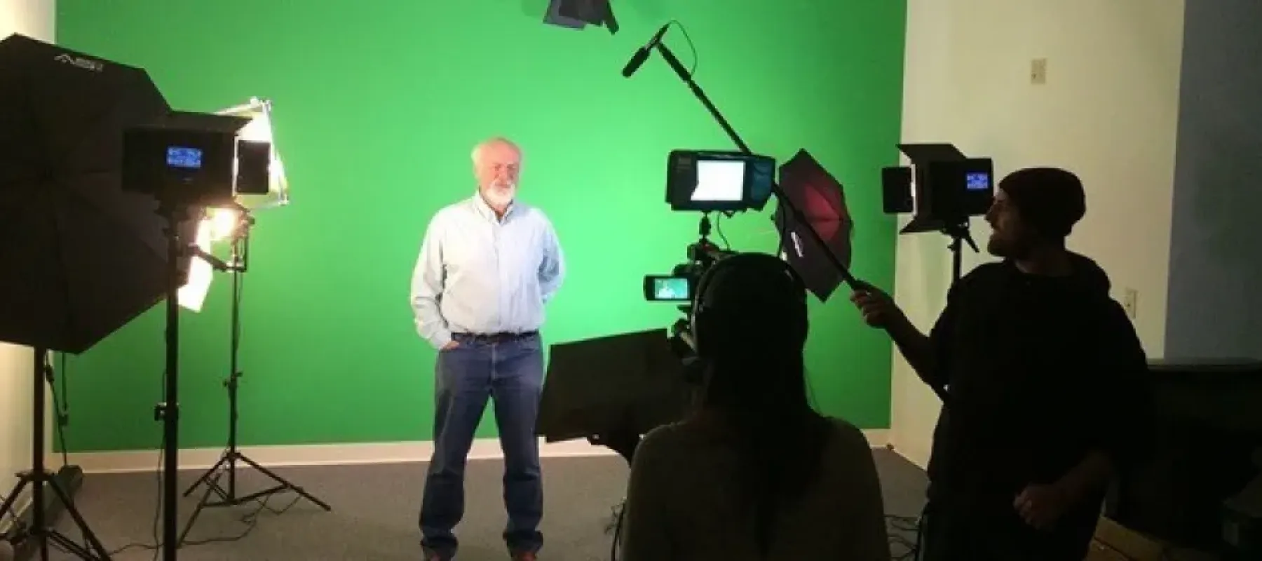 Man standing in front of green screen with two other people recording.