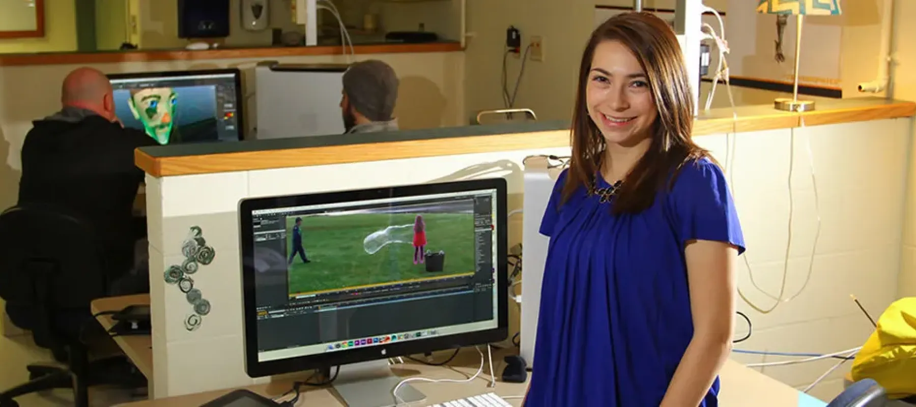 Student posing next to computer with video editing software on screen.
