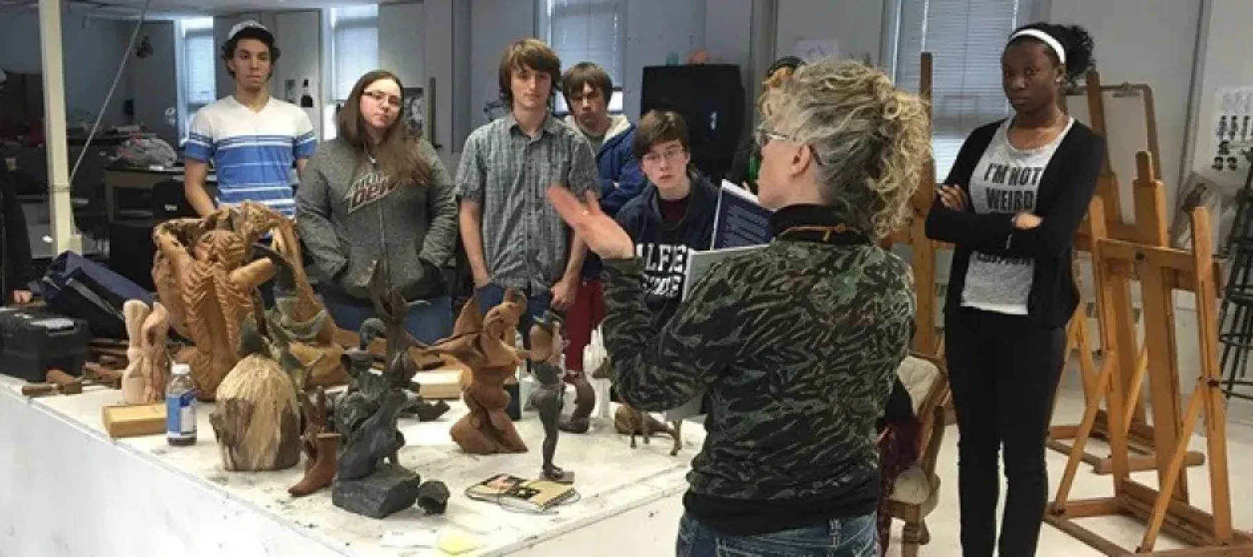Students listening to professor in classroom with sculptures on table.