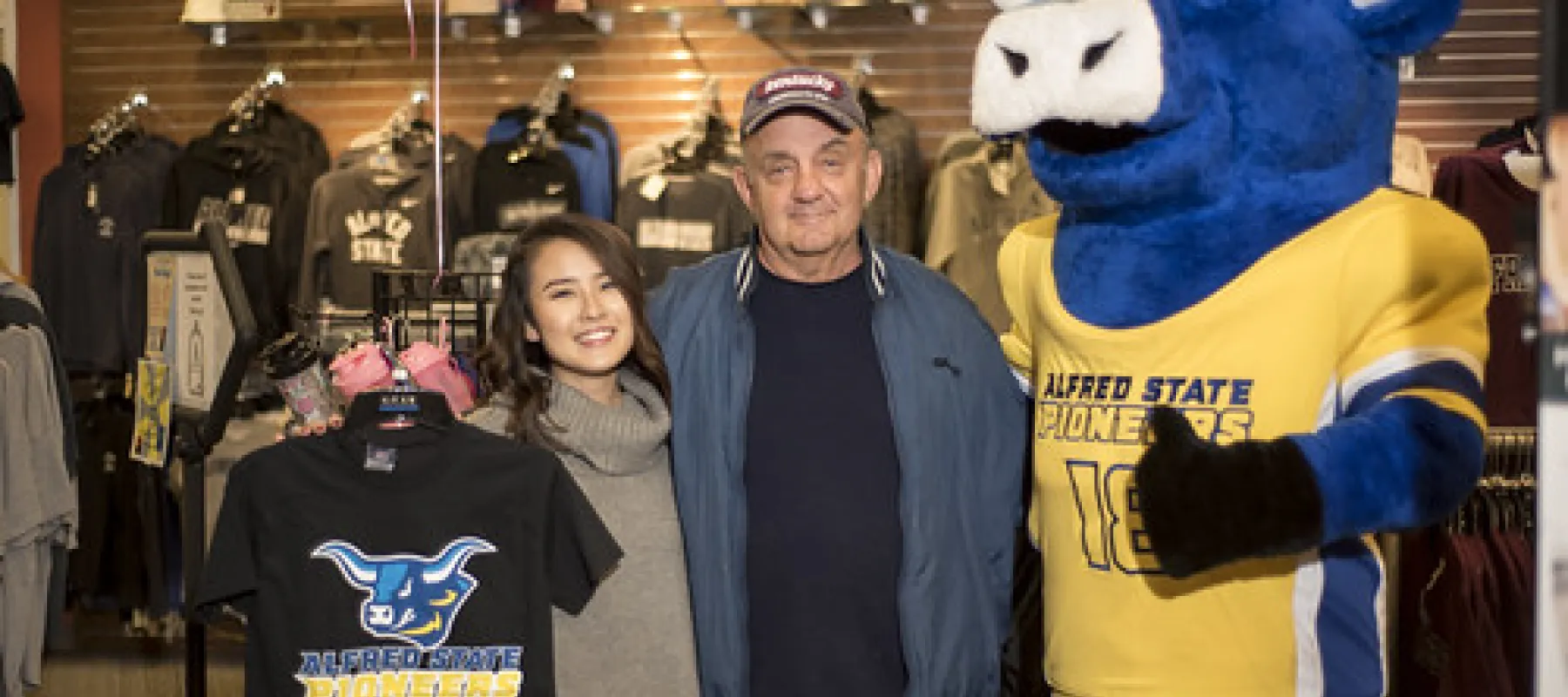 Big Blue posing with a man and woman inside the campus store.