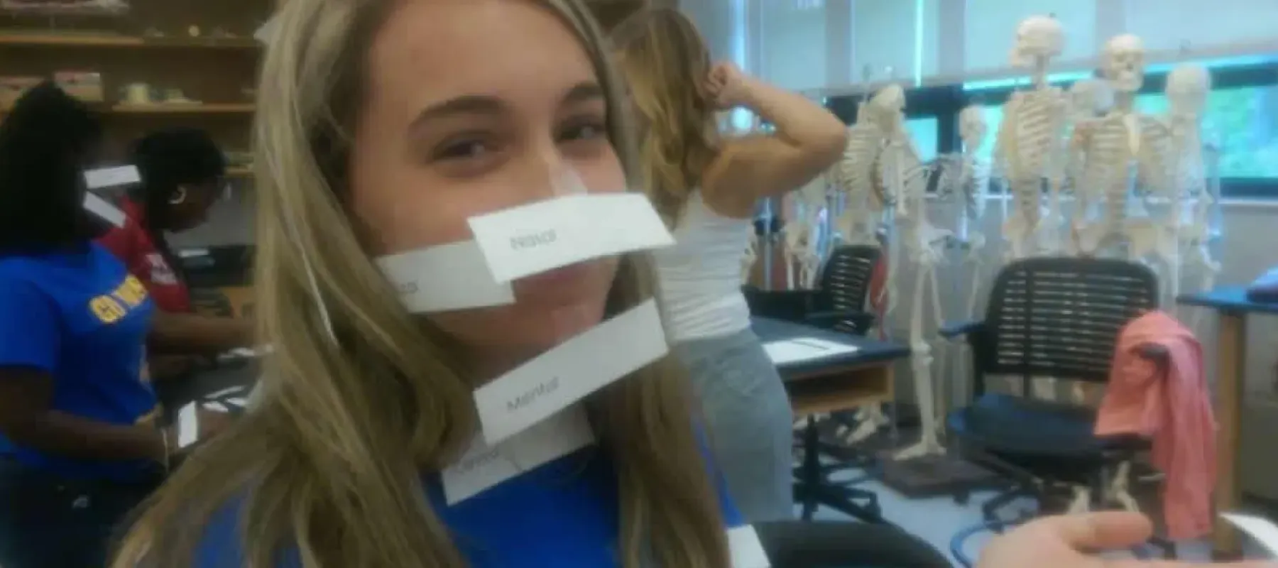 Student in lab with notice attached to face with names of different parts of the body.