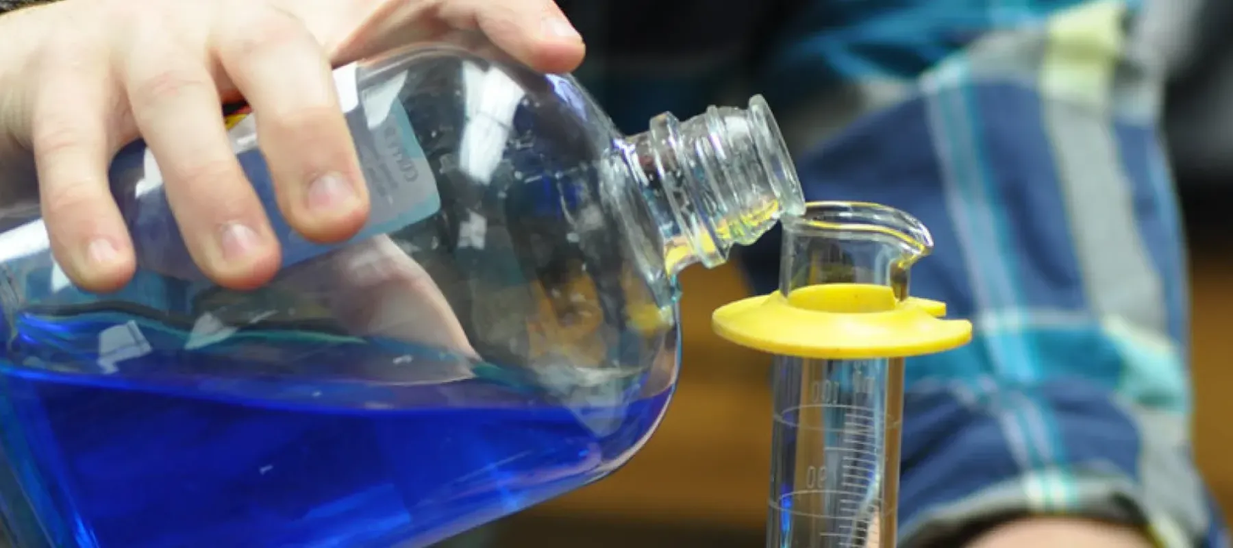 Student pouring blue liquid into beaker.