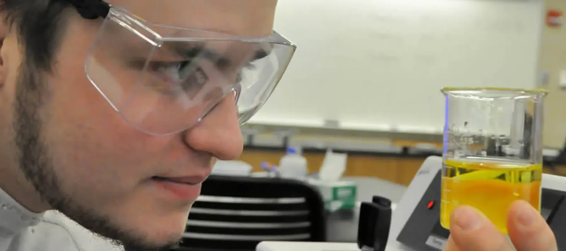 Student looking at yellow liquid in beaker.