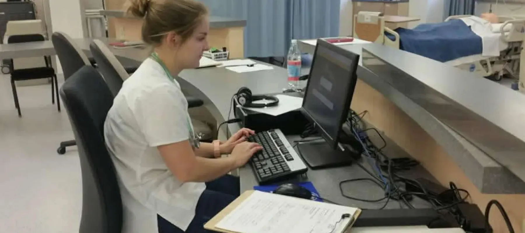 Healthcare management student working on computer at desk in hospital environment.