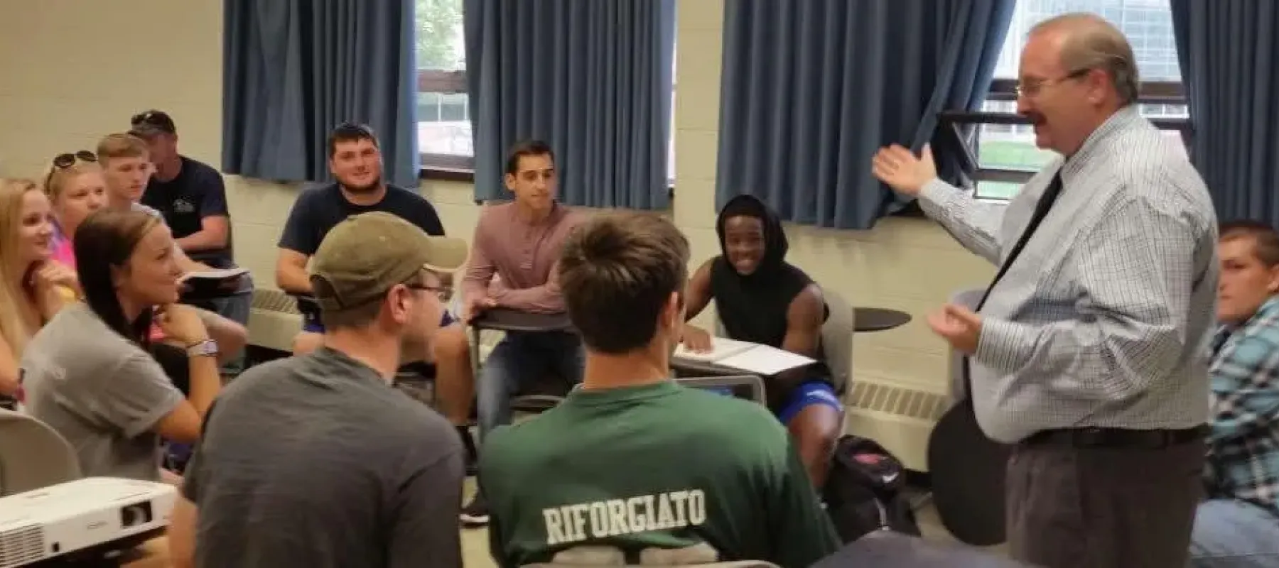 Students sitting at desks in classroom listen to professor.