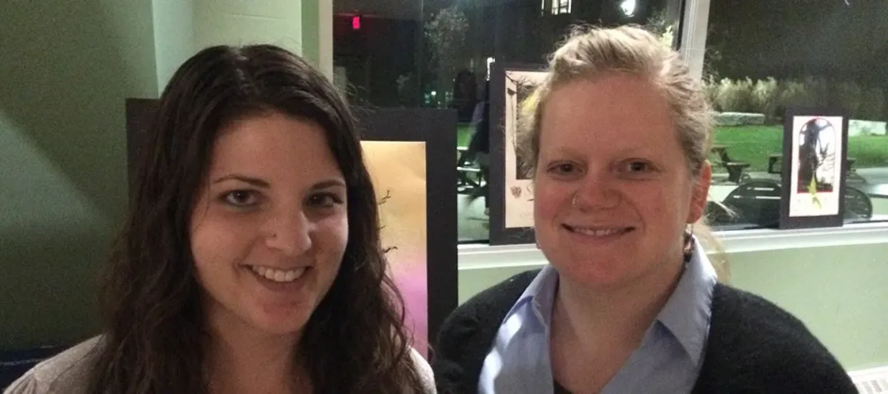 Two woman posing for photo inside.