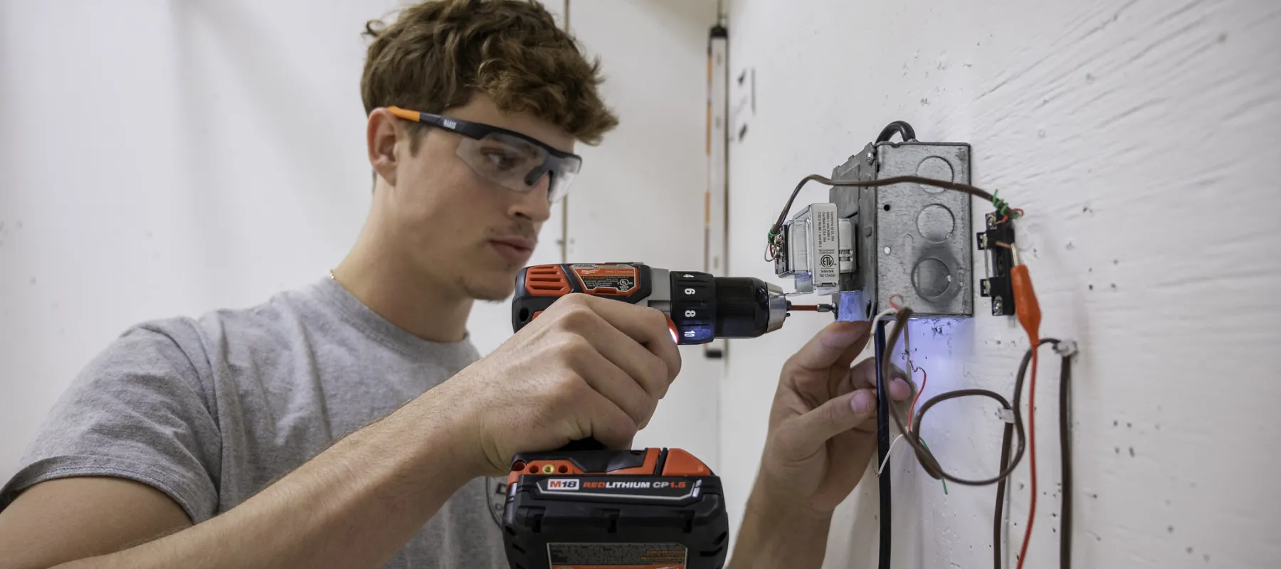 Electrical Construction and Maintenance Electrician student working on wiring device on wall.