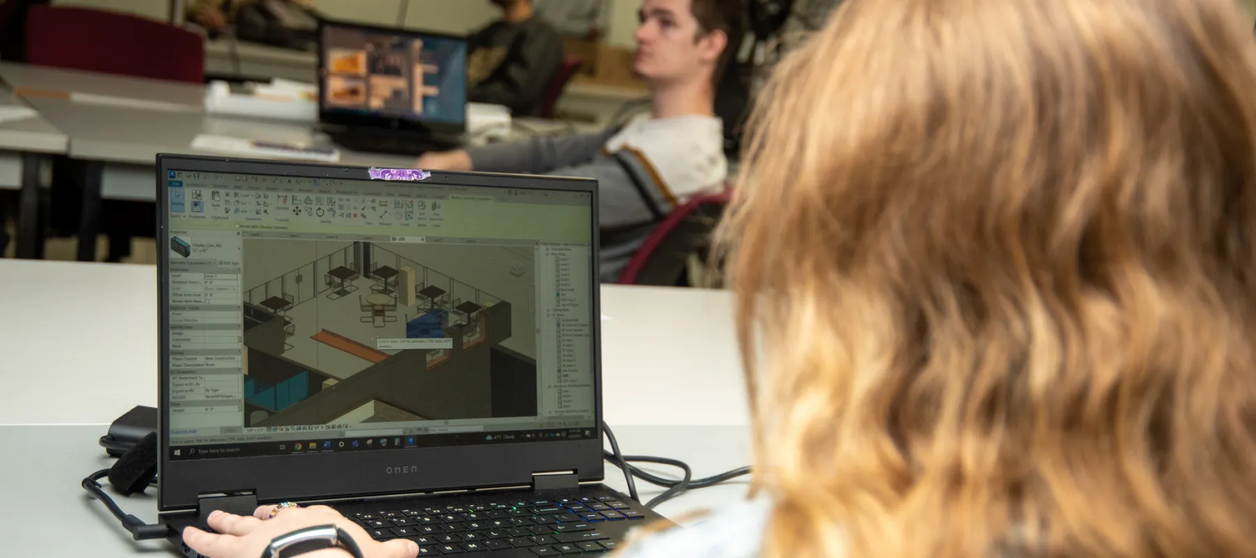 Student working on laptop with CAD software visible.
