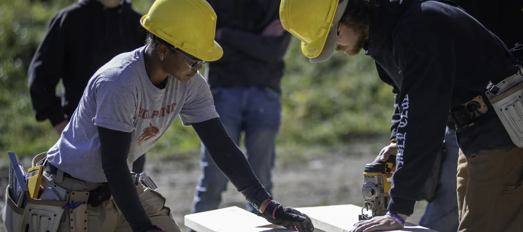 Two students cutting boards on a construction site.