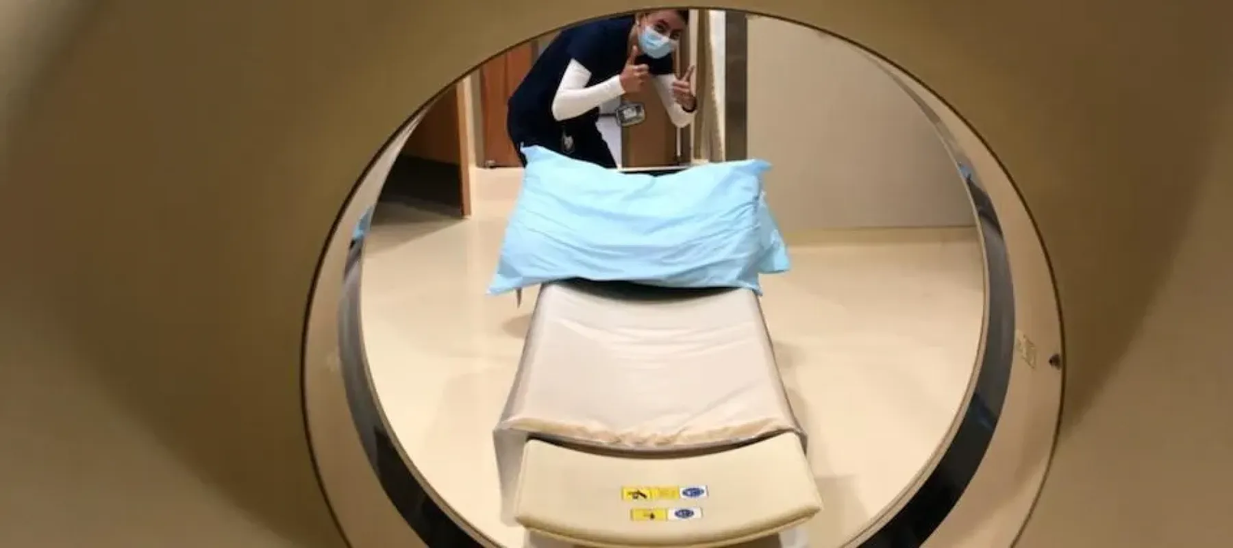 Picture taking from inside MRI machine looking out at student with thumbs up.