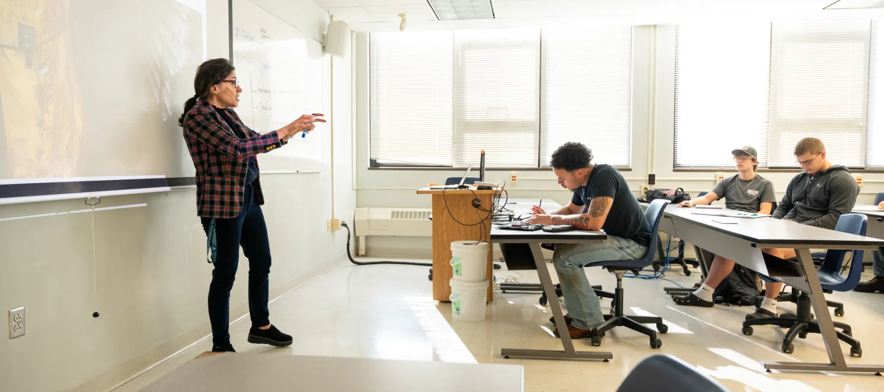 Civil engineering technology students taking notes in class with professor teach at the front of the room.