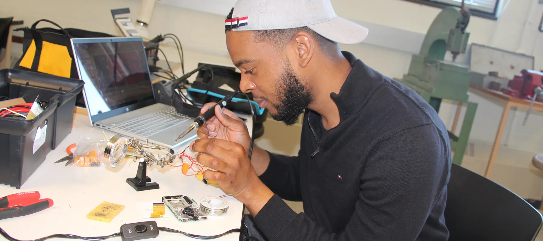 Computer engineering student soldering wires to electrical component.