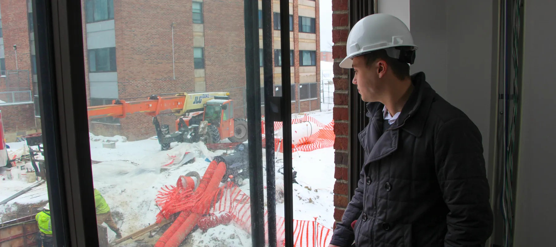 Man with hard hat looking out window at construction site.
