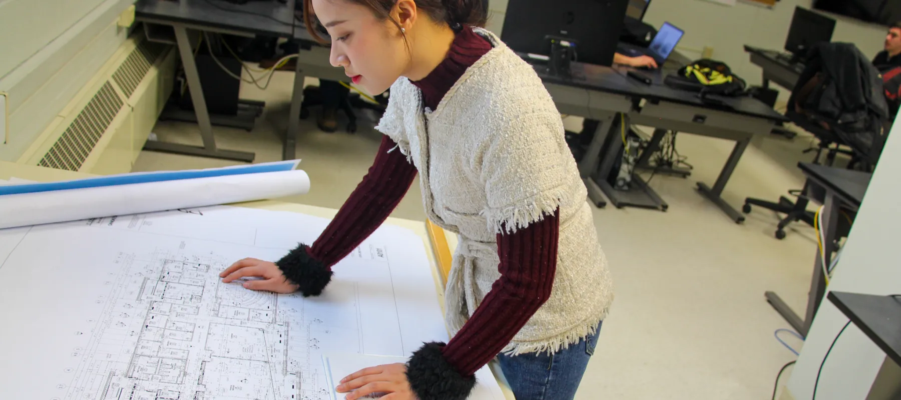 Construction management student in classroom looking at building plans.