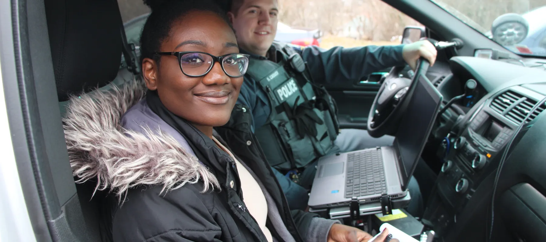 Criminal justice student sitting with police officer in car.