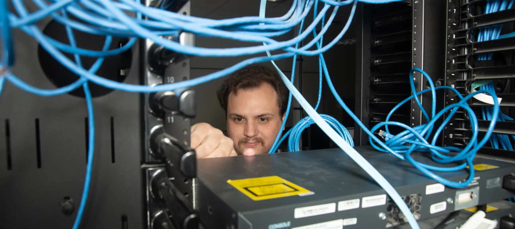 Cyber security student working on network rack in lab.