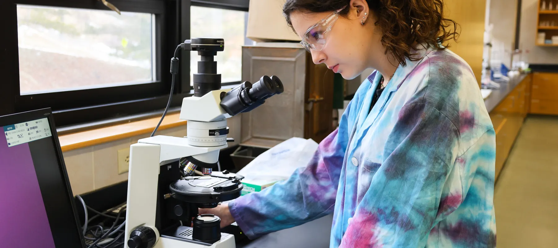 A student looking through a microscope in a lab.